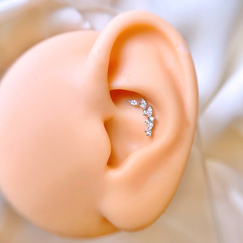 Op de afbeelding: Een zilveren gebogen barbell met een rij heldere zirkonia-stenen, gedragen in een helix piercing.