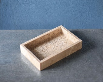 May include: A rectangular tray made of light brown travertine stone. The tray has a smooth, slightly textured surface and a raised rim.