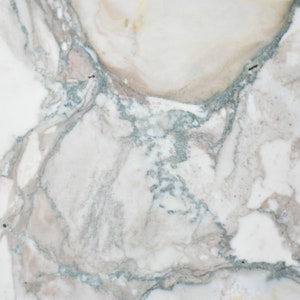 May include: Close-up of a white marble surface with grey and brown veining. The marble has a smooth, polished finish.