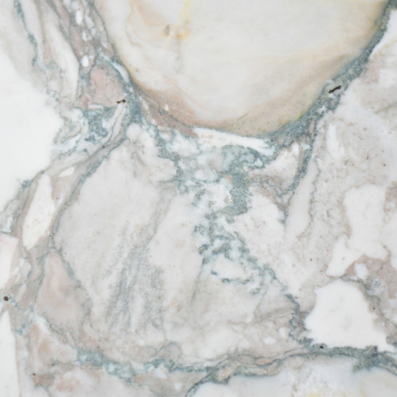 May include: Close-up of a white marble surface with grey and brown veining. The marble has a smooth, polished finish.