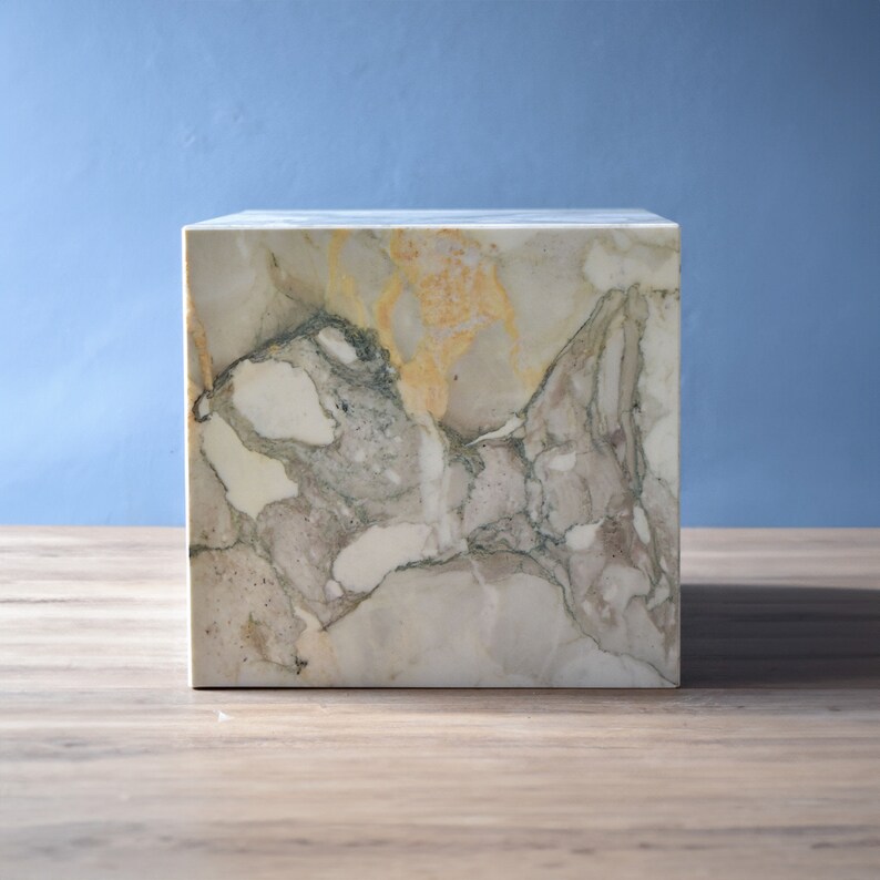 May include: A square, white marble side table with a unique, swirling pattern of grey, white, and yellow veins.