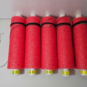 May include: Five red foam pool noodles with black straps and yellow reflective tape. The noodles are hanging from a white ceiling.