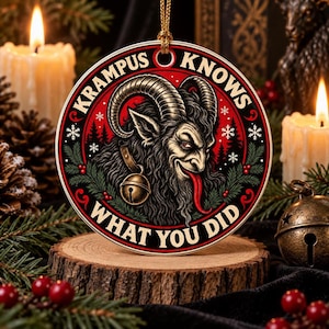 Può includere: Un addobbo natalizio rotondo con un'illustrazione dettagliata di Krampus con grandi corna, una lunga lingua rossa e un collare con campanello. Il design presenta uno sfondo rosso e nero con rami di pino, fiocchi di neve e il testo KRAMPUS KNOWS WHAT YOU DID.