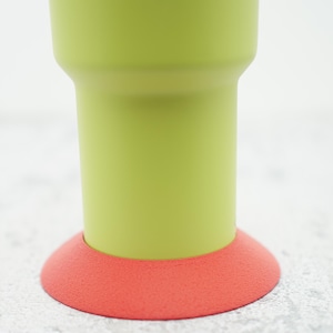 Puede incluir: Un vaso verde lima con una base de goma naranja brillante. La base está diseñada para proteger las superficies de los arañazos.