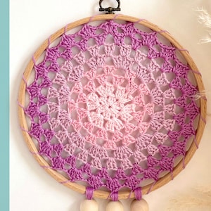 May include: A handmade dreamcatcher with a crochet pattern in shades of pink and purple. The crochet design is centered within a wooden hoop, with wooden beads hanging below. The word "PATTERN" is written vertically on the left side.