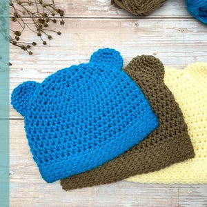 May include: Three crocheted hats with bear ears. The hats are blue, brown, and yellow.