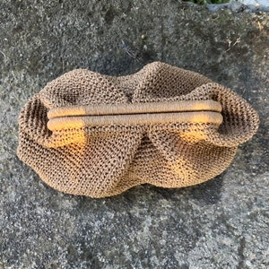May include: A brown crocheted bag with a woven handle. The bag is made of a fine, textured material and has a slightly rounded shape.
