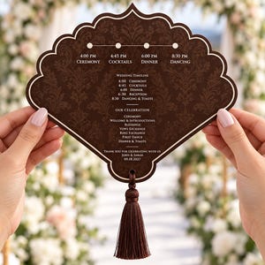 May include: A dark brown fan-shaped wedding program with a white border and a matching tassel. The text includes a timeline with events like Ceremony, Cocktails, Dinner, and Dancing, plus a detailed schedule for John and Sarah on 09.18.2027.