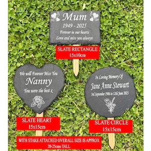 May include: Three slate memorial garden markers with wooden stakes. The markers are in rectangle, heart, and circle shapes. The rectangle reads "Mum 1949-2025". The heart says "Nanny". The circle says "In Loving Memory of Jane Anne Stewart".