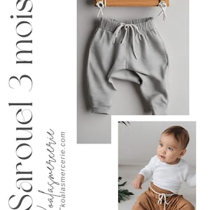 Può includere: Pantaloni della tuta grigi e marroni per neonato con coulisse bianca. I pantaloni della tuta sono appesi a un appendiabiti di legno e un bambino indossa i pantaloni della tuta marroni.