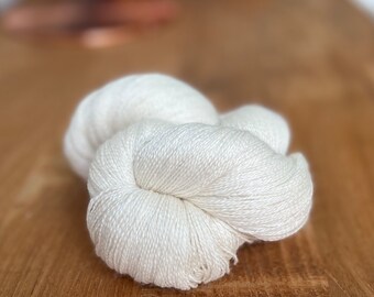 May include: A skein of white yarn, made of natural fibers, is shown on a wooden surface. The yarn is soft and fluffy, and it is perfect for knitting or crocheting.
