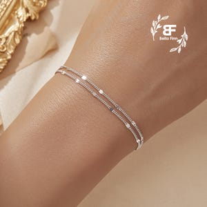 以下が含まれることがあります： 小さな楕円形のリンクを特徴とする繊細なデザインのシルバーチェーンブレスレット。ブレスレットは2つのチェーンを重ねており、スタイリッシュでモダンなルックを生み出しています。