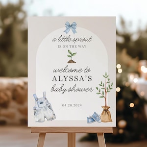 May include: A baby shower welcome sign for Alyssa, with watercolour illustrations of baby clothes, a sapling, and shoes. The sign says "a little sprout is on the way" and includes the date 04.20.2024. The sign is displayed on a wooden easel.