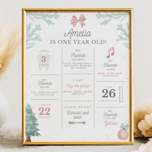 May include: A printable Christmas-themed first birthday chart for a girl named Amelia. The chart includes details about her favorite things, what she can do, and her measurements. It features a festive green and red color scheme with a cute illustration of a Christmas tree.