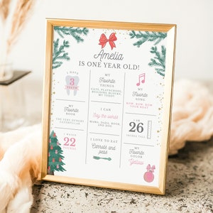 May include: A festive Christmas-themed printable poster for a one-year-old girl named Amelia. The poster features a Christmas tree, a tooth, a measuring tape, and a musical note. It includes details about Amelia's favorite things, like her favorite book, song, and food. The poster is decorated with a red bow and gold glitter.