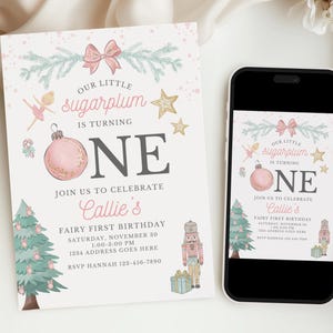 May include: A printed birthday invitation and a smartphone displaying the same digital invitation. The design features a pink ornament, a nutcracker, a Christmas tree, a ballerina, and gold stars with the text Our Little Sugarplum Is Turning One.