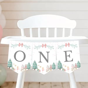 May include: A white high chair banner featuring three pennants with the letters O, N, and E in grey. The design includes illustrations of pink bows, green pine branches, Christmas trees, nutcrackers, rocking horses, and ballerinas.