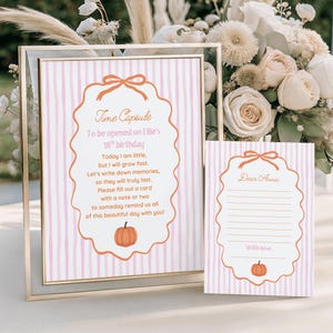May include: A vertical sign in a gold frame and a matching card featuring a light pink and white striped background. Both items display an orange scalloped border with a bow at the top and a pumpkin at the bottom. The sign reads Time Capsule.