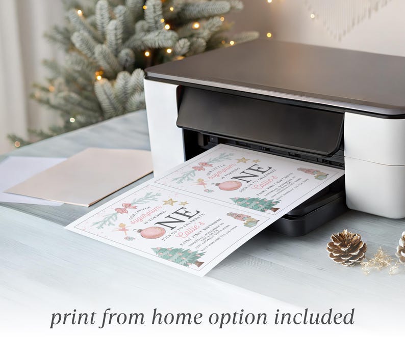 May include: A white and black home printer outputting two identical rectangular paper invitations. The invitations feature pink and green holiday-themed graphics, including a Christmas tree, ornaments, and the text Our Little Sugarplum Is Turning ONE.