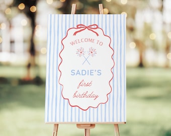 Pode incluir: Um letreiro de boas-vindas para uma primeira festa de aniversário. O letreiro apresenta um fundo branco com listras verticais azuis. O texto "WELCOME TO SADIE'S first birthday" é exibido em vermelho e azul dentro de uma borda vermelha decorativa.