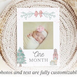 May include: A rectangular milestone card featuring a central photo of a baby wearing a pink flower headband. The card is decorated with a pink bow, pine branches, a Christmas tree, a nutcracker, and the text One MONTH in gray lettering.