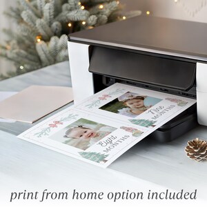 May include: A white and black home printer outputting a sheet of paper featuring two photo milestone cards. Each card displays a baby's portrait, festive holiday illustrations, and the text Eight Months and Nine Months in cursive script.
