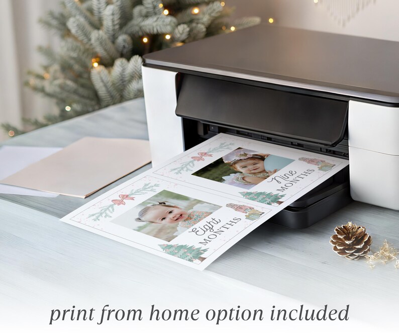 May include: A white and black home printer outputting a sheet of paper featuring two photo milestone cards. Each card displays a baby's portrait, festive holiday illustrations, and the text Eight Months and Nine Months in cursive script.