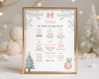 May include: A framed milestone poster for a one-year-old named Helena, featuring pink and green holiday graphics like pine branches, a Christmas tree, and a bow. The text details her age, 3 teeth, 26 inches tall, and 22 pounds in weight.