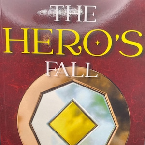 May include: A book cover with a red background and gold accents. The title is "The Hero's Fall" in yellow letters. The subtitle is "A Chronicle of Valsavia and Almaría" in white letters. The author's name is "Kirt Winter" in yellow letters.
