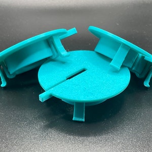 Może przedstawiać: Trzy turkusowe plastikowe osłony z rozciętym wzorem. Osłony mają zaokrąglony kształt i podniesioną krawędź wokół krawędzi. Osłony są zaprojektowane tak, aby pasowały do okrągłego otworu.