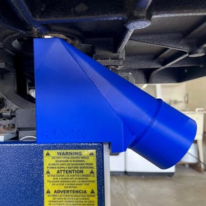 May include: A blue plastic bandsaw dust collection port attached to a machine. The port is angled and has a cylindrical outlet. A warning label is visible with safety instructions. The text "R 10-326" is also visible.