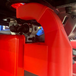 May include: Close-up of a red power tool with a black and silver mechanism. The tool has a protective guard and a black handle.