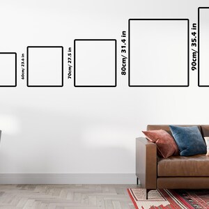 K&ouml;nnte beinhalten: Sechs gerahmte Kunstwerke in verschiedenen Gr&ouml;&szlig;en, von 40 cm bis 90 cm, an einer wei&szlig;en Wand. Die schwarzen Rahmen sind mit cm und Zoll beschriftet. Im Vordergrund ist ein braunes Ledersofa mit Kissen zu sehen, links ein Schreibtisch und ein Stuhl.