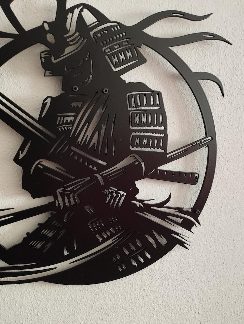 K&ouml;nnte beinhalten: Schwarze Metall-Wandkunst, die einen Samurai-Krieger in voller R&uuml;stung mit gekreuzten Schwertern darstellt. Das Kunstwerk ist als Silhouette geschnitten, mit komplizierten Details im Helm und in der R&uuml;stung. Der Samurai ist in einem kreisf&ouml;rmigen Rahmen angeordnet.
