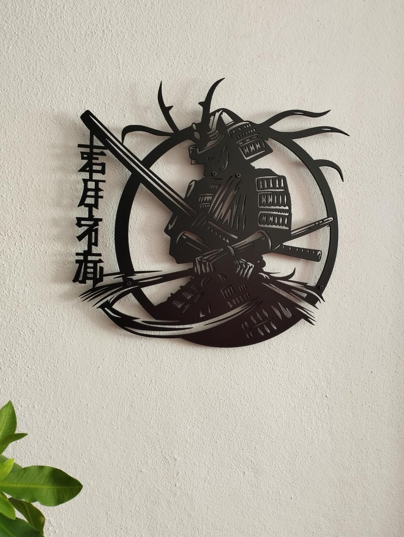 K&ouml;nnte beinhalten: Schwarze Metall-Wandkunst, die einen Samurai-Krieger in einem kreisf&ouml;rmigen Rahmen darstellt. Das Kunstwerk zeigt detaillierte Merkmale der R&uuml;stung, Schwerter und des Helms des Samurai. Japanische Schriftzeichen sind vertikal auf der linken Seite platziert. Die Kunst ist an einer wei&szlig;en Wand befestigt.