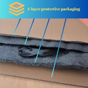 K&ouml;nnte beinhalten: Sch&uuml;tzende Verpackung mit vier Schichten, bestehend aus Pappe und dunkelgrauem Schaumstoff. Ein schwarzes dekoratives Objekt ist im Schaumstoff sichtbar. Das Bild enth&auml;lt den Text "4-layer protective packaging".