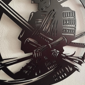 K&ouml;nnte beinhalten: Schwarze Metall-Wandkunst, die einen Samurai-Krieger im Profil zeigt, der ein Katana h&auml;lt. Das Kunstwerk ist aus einem einzigen Metallblech geschnitten und zeigt detaillierte Darstellungen der R&uuml;stung und des Helms. Der Samurai befindet sich in einem kreisf&ouml;rmigen Rahmen.