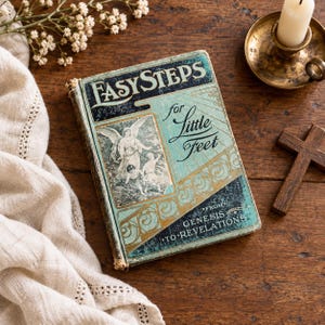 May include: An antique hardcover book titled Easy Steps for Little Feet from Genesis to Revelations. The cover features a teal and gold color scheme with a black and white illustration of an angel and children, ornate scrollwork, and worn edges.
