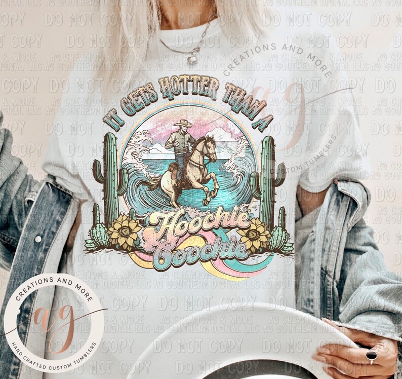 May include: A white t-shirt with a graphic design featuring a cowboy riding a horse through a wave with the text "It gets hotter than a Hoochie Coochie". The design also includes cacti and sunflowers.