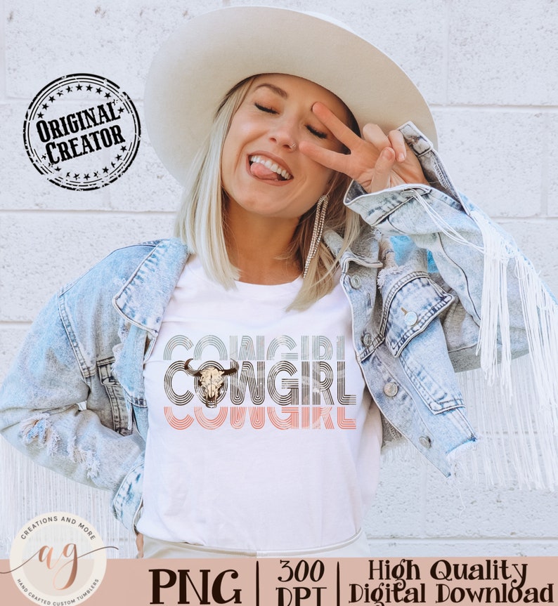 May include: A white t-shirt with a graphic design of the word "COWGIRL" repeated three times in a retro style with a cow skull in the center. The shirt is being worn by a person with blonde hair and a white cowboy hat.