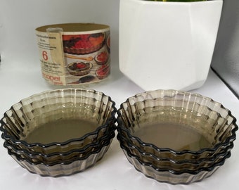 May include: Six brown glass ramekins with scalloped edges stacked in two sets of three. The ramekins are on a white surface.