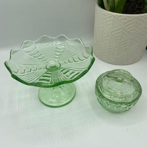 May include: Two vintage green glass dishes. One is a pedestal dish with a scalloped edge and the other is a round dish with a lid.
