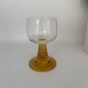 Könnte beinhalten: Ein klares Weinglas aus Glas mit einem braunen, strukturierten Stiel und Fuß.