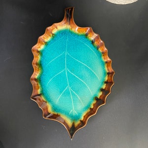 May include: A teal blue ceramic leaf-shaped serving dish with a brown rim and a raised vein pattern.
