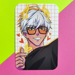 Può includere: Un adesivo rettangolare raffigurante un personaggio in stile anime con capelli bianchi, occhiali arancioni e una maglietta nera. Il personaggio sorride e forma un cuore con le dita. Lo sfondo ha un motivo a griglia e piccoli cuori rossi.
