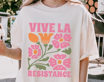 May include: A white oversized t-shirt with a pink and green floral design and the text "VIVE LA RESISTANCE" printed on the front.