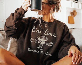 Może przedstawiać: Brązowa bluza z nadrukiem "tini time" i grafiką kieliszka do martini z wymienionymi składnikami: wódka, espresso, likier kawowy, espresso martini.