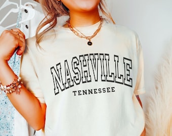 May include: A light yellow t-shirt with a black graphic that says "NASHVILLE TENNESSEE" in a collegiate font.