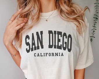 May include: A cream colored t-shirt with black text that reads "SAN DIEGO CALIFORNIA".