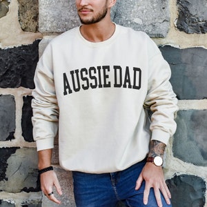 May include: A beige sweatshirt with the text "Aussie Dad" printed in black on the front.